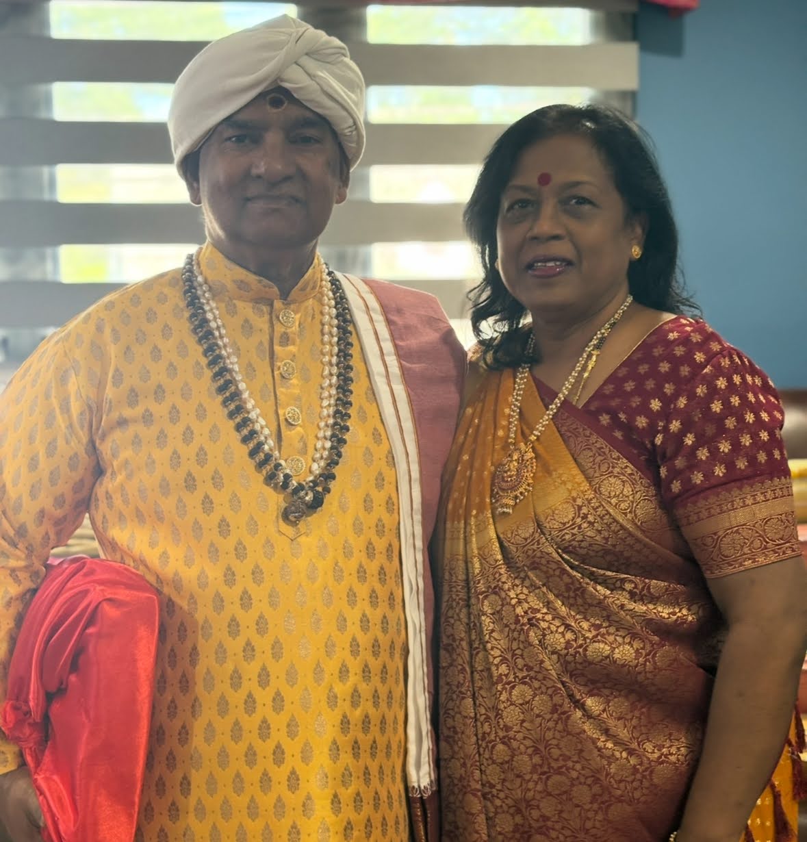 Pandit Mahendranauth Doobay in a cream turban and gold kurta, standing beside a woman in a maroon and gold sari