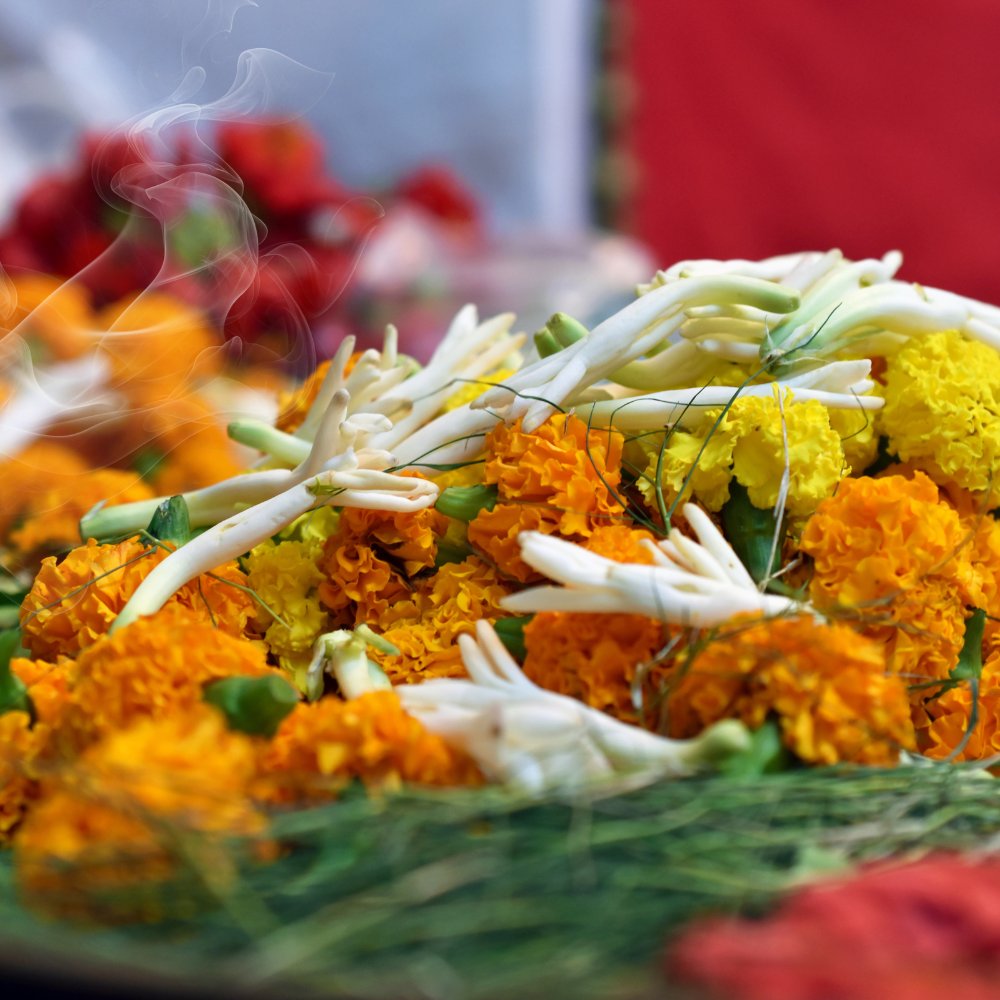 Marigolds and white flowers with incense smoke, arranged as a puja offering
