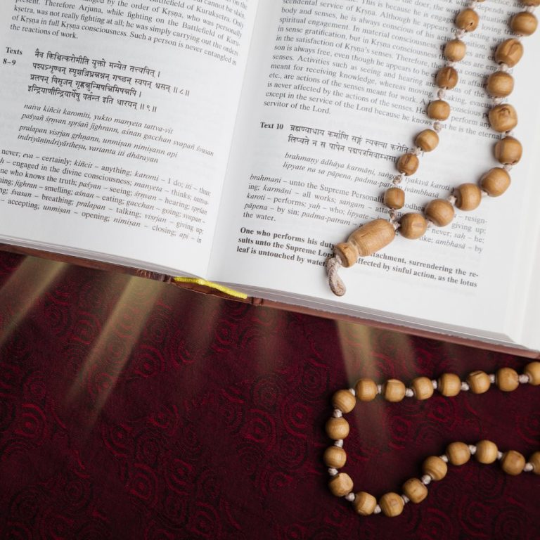 Open scripture with Sanskrit verses and wooden prayer beads on a red cloth